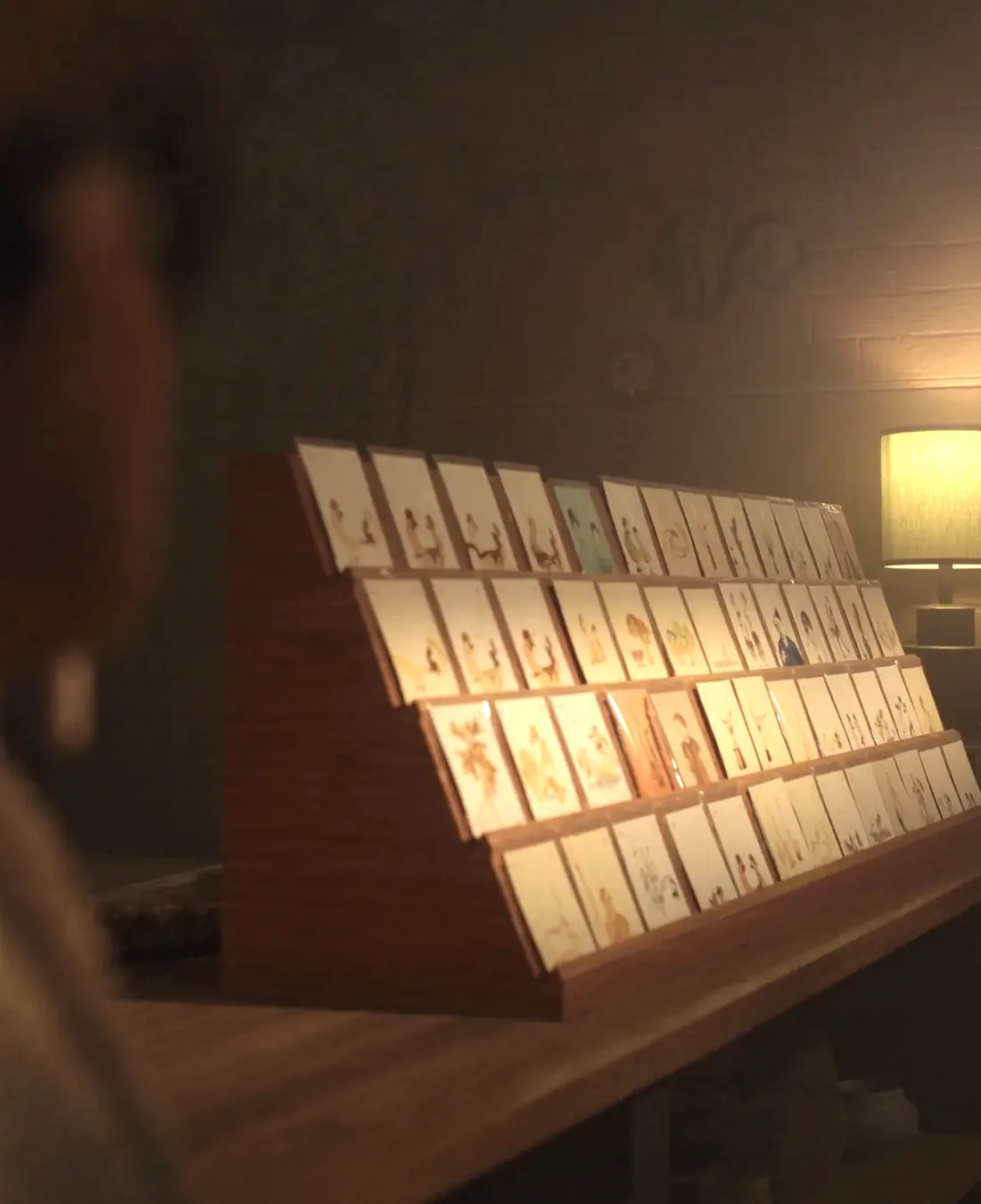 A wooden greeting card rack in a small shop, cards standing upright in rows in their sleeves, with a brick wall behind and warm lamp light.