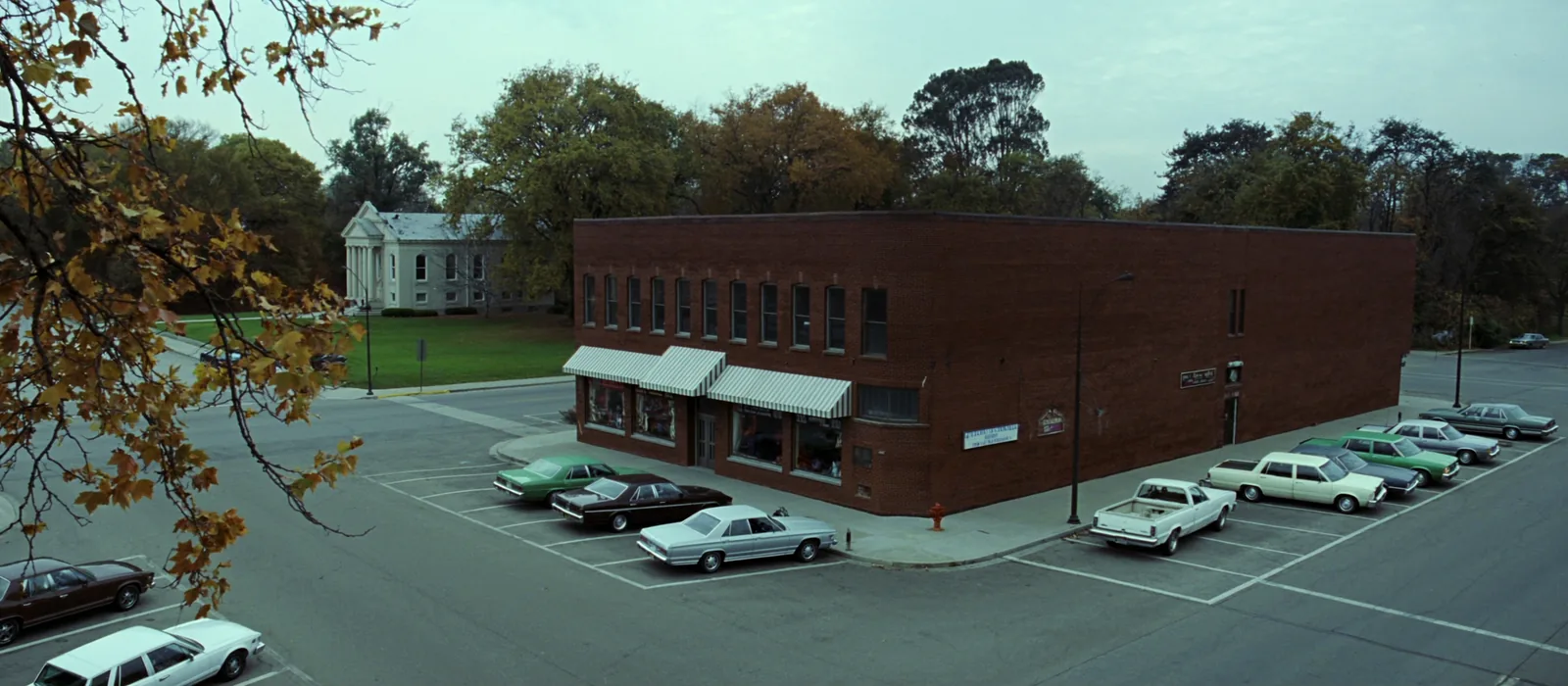 A small Missouri county courthouse square in autumn, with a limestone courthouse set back on a lawn among turning trees and two storey brick storefronts facing it across angled parking.